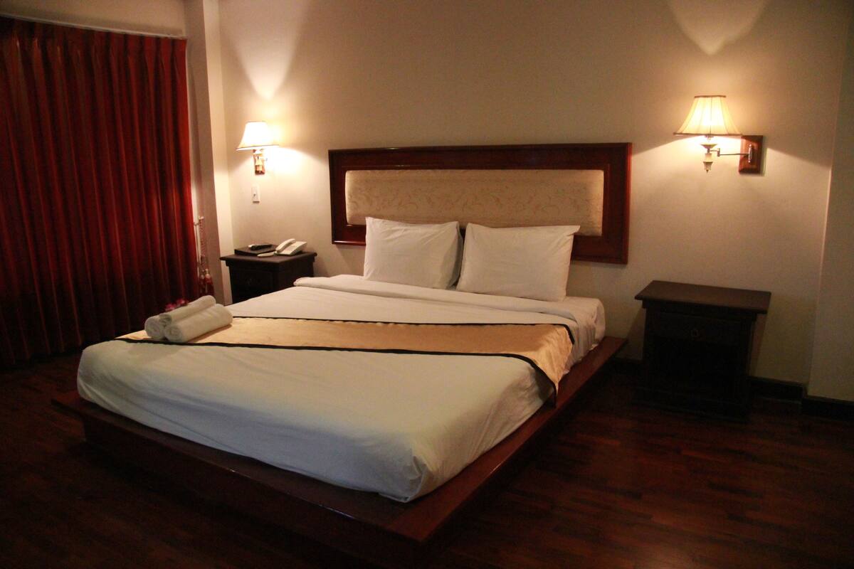 A hotel room with a large bed, two bedside lamps, a nightstand, and a red curtain.