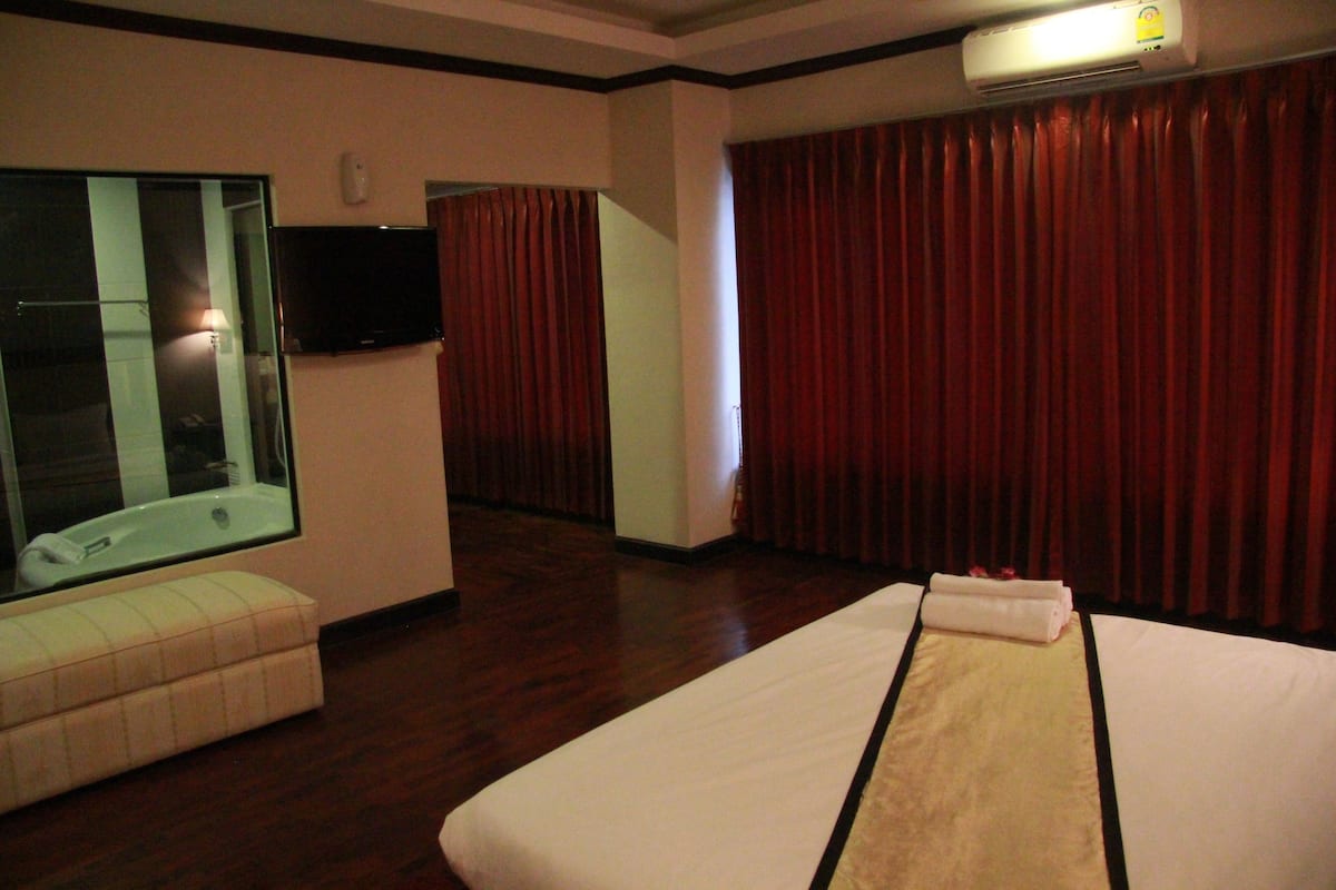 A hotel room with a large bed, a small sofa, a TV, and a window with curtains.