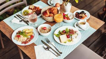 Ett frukostbord med tallrikar fulla av mat, en korg med croissanter och en kopp kaffe.