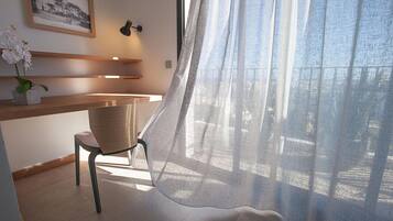 A modern room with a wooden desk, a chair, a potted orchid, a framed picture on the wall, and a sheer curtain.
