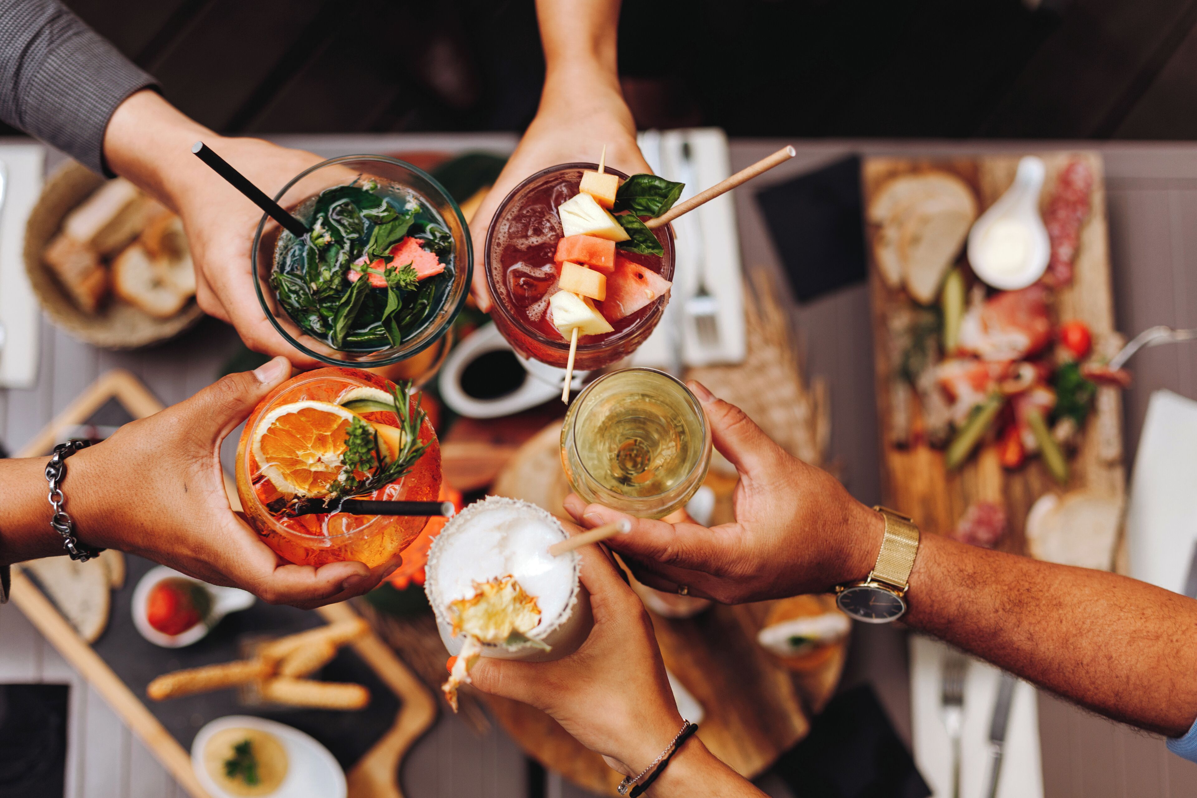 A group of people holding various drinks, likely cocktails, with garnishes and straws.