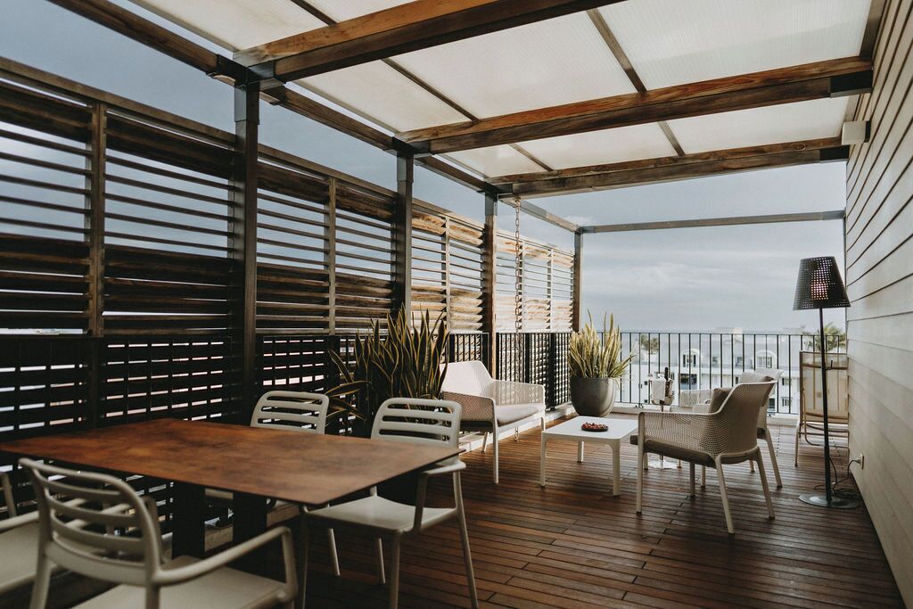 An outdoor patio with a wooden table and chairs, a white sofa, and a potted plant.