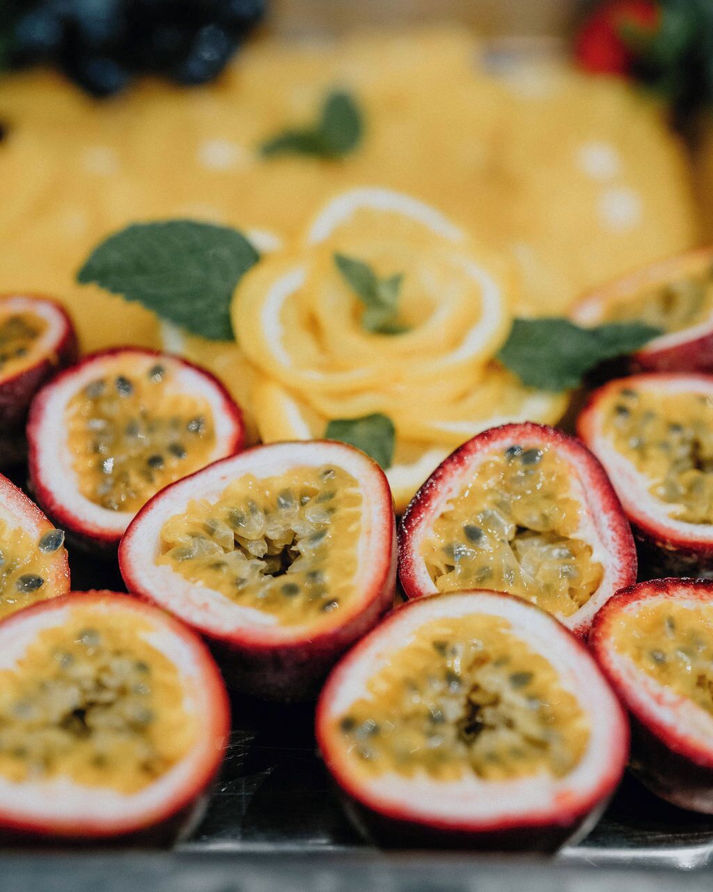 Ein Detailbild von passioniertem Obst und einer gelben Frucht, möglicherweise Mango, angeordnet auf einer Oberfläche mit grünen Blättern.