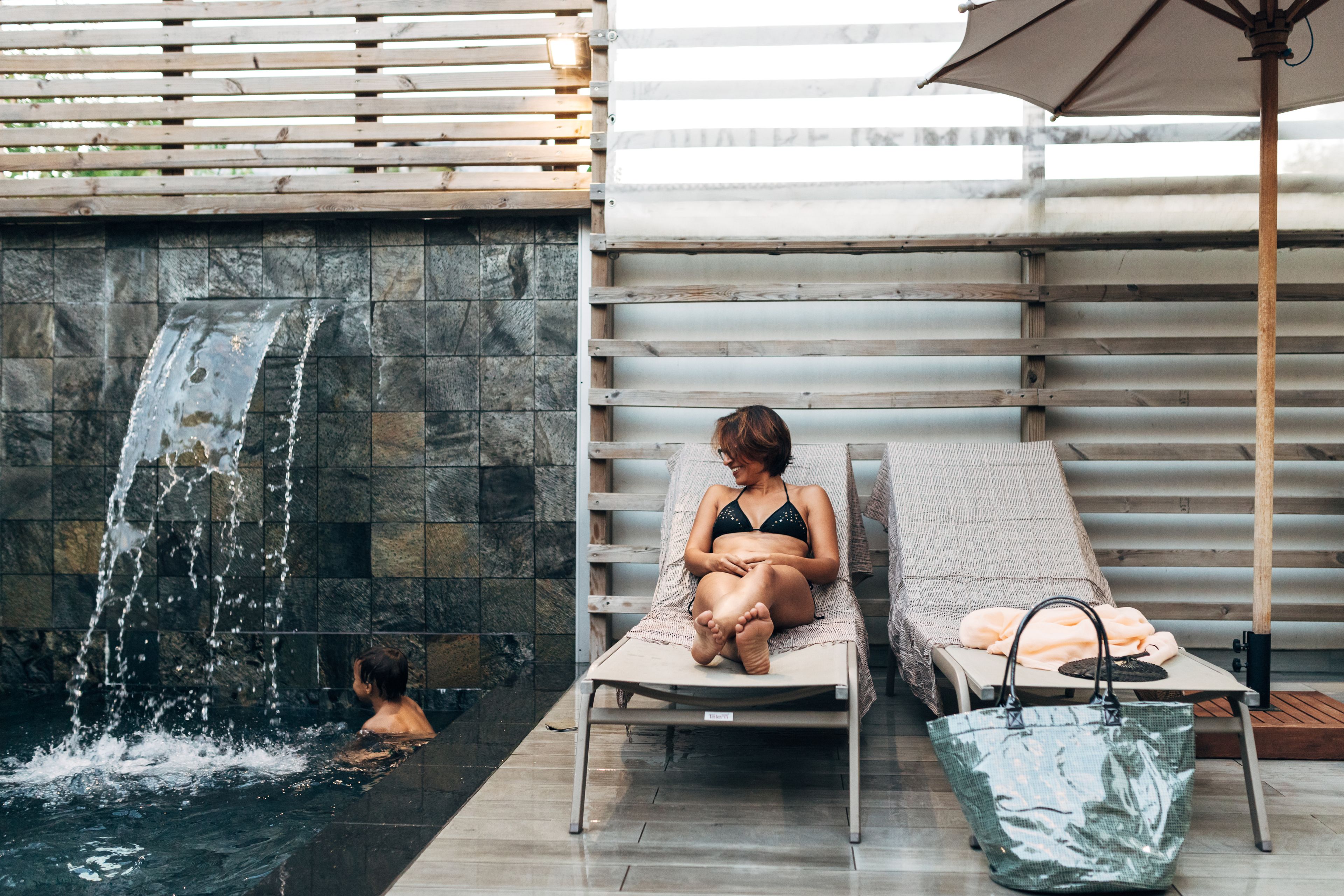 A spa area with a water feature, lounge chairs, and a table with a bag.