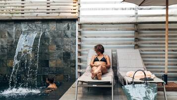 A spa area with a water feature, lounge chairs, and a table with a bag.