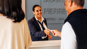A hotel reception area with a receptionist, a guest, and a man handing over a card. - Le Saint Pierre Hotel (Saint-Pierre)