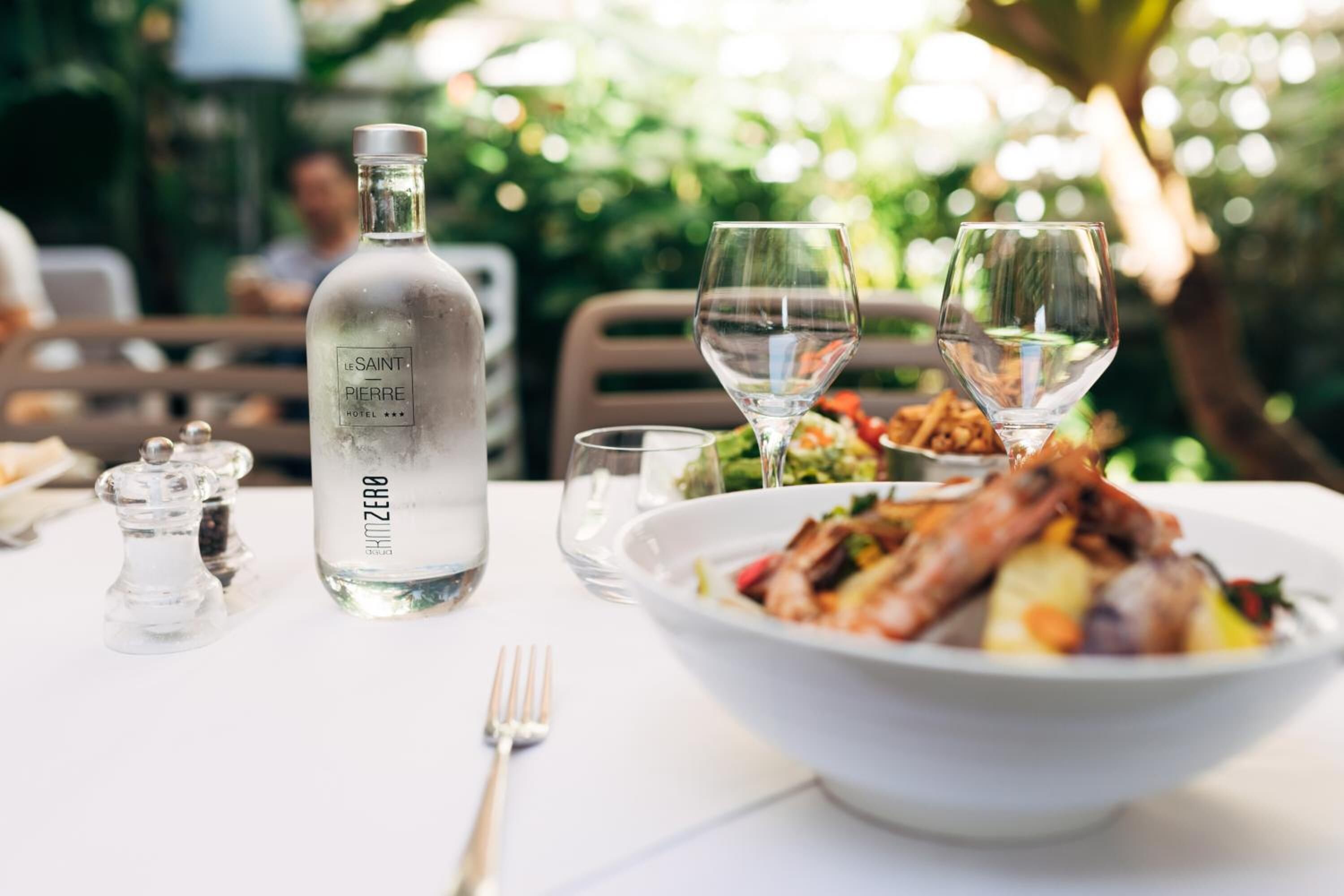 Un tavolo da pranzo con una bottiglia d'acqua dell'Hotel Saint-Pierre, due bicchieri da vino e una ciotola di cibo.