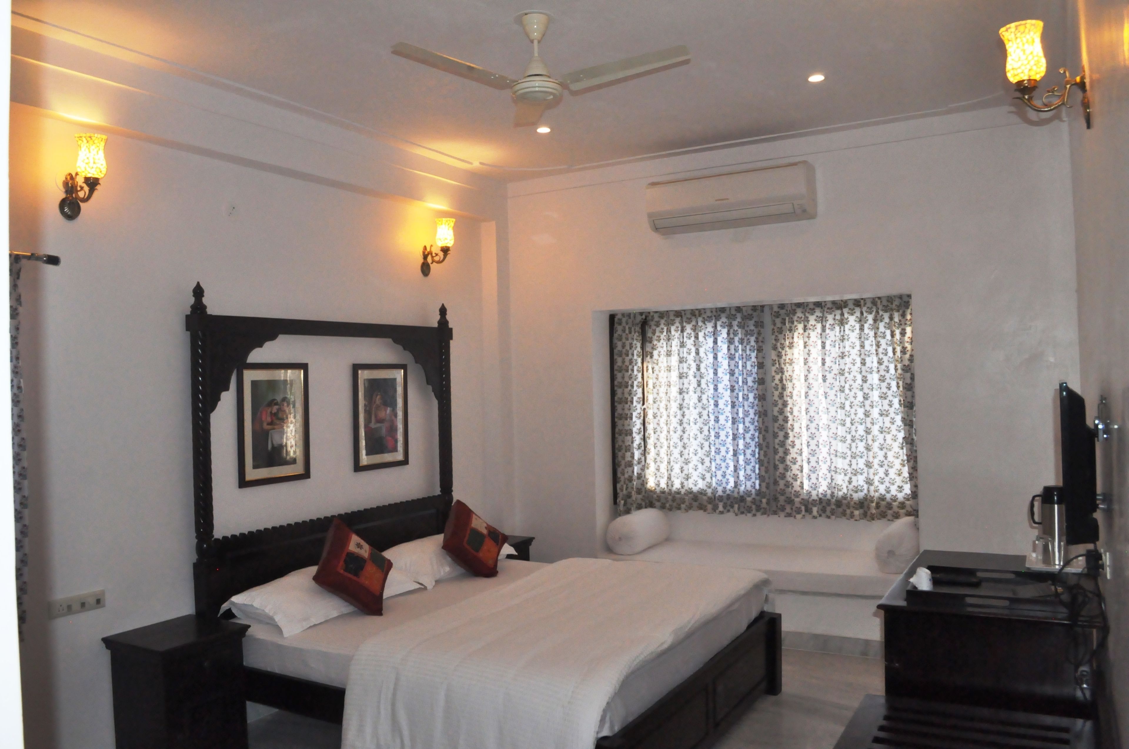 Quarto com uma cama grande, mesa de cabeceira, ventilador de teto e janela com cortinas.
