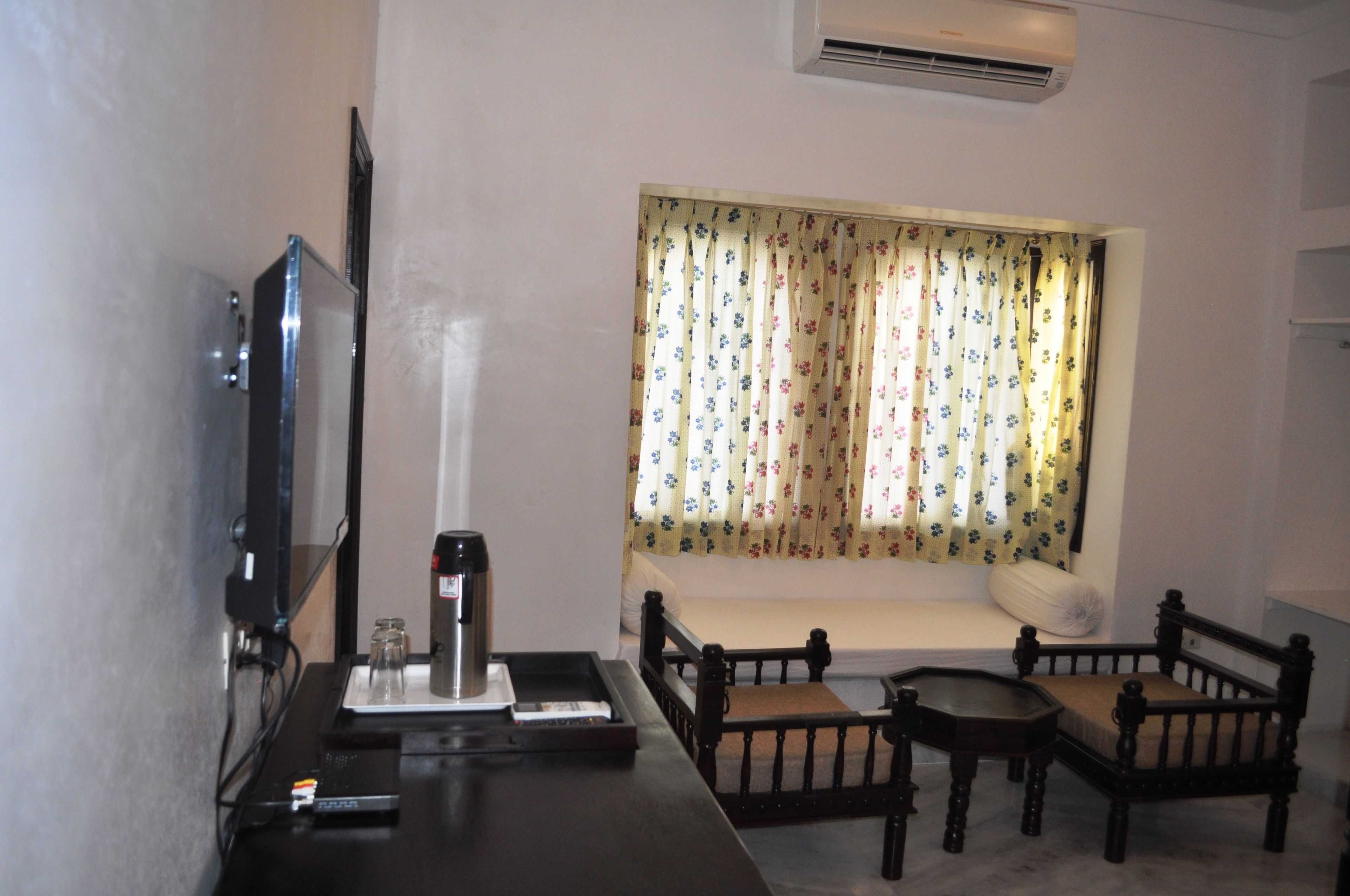 A room with a bed, a TV, a coffee maker, and a window with floral curtains.