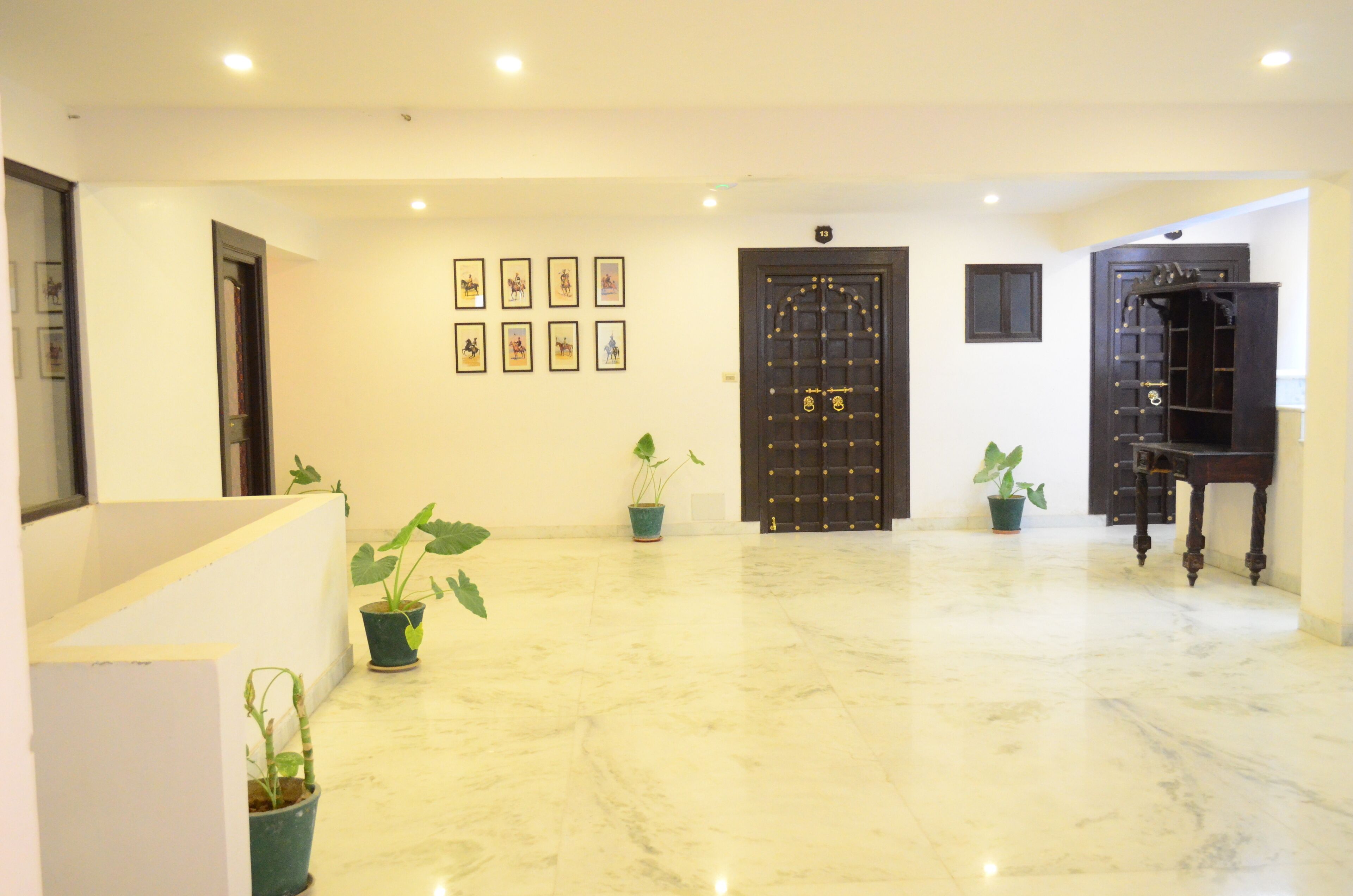A spacious lobby with a marble floor, a black ornate door, and several potted plants.
