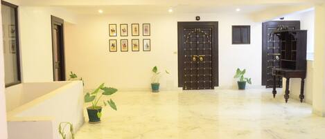 A spacious lobby with a marble floor, a black ornate door, and several potted plants.
