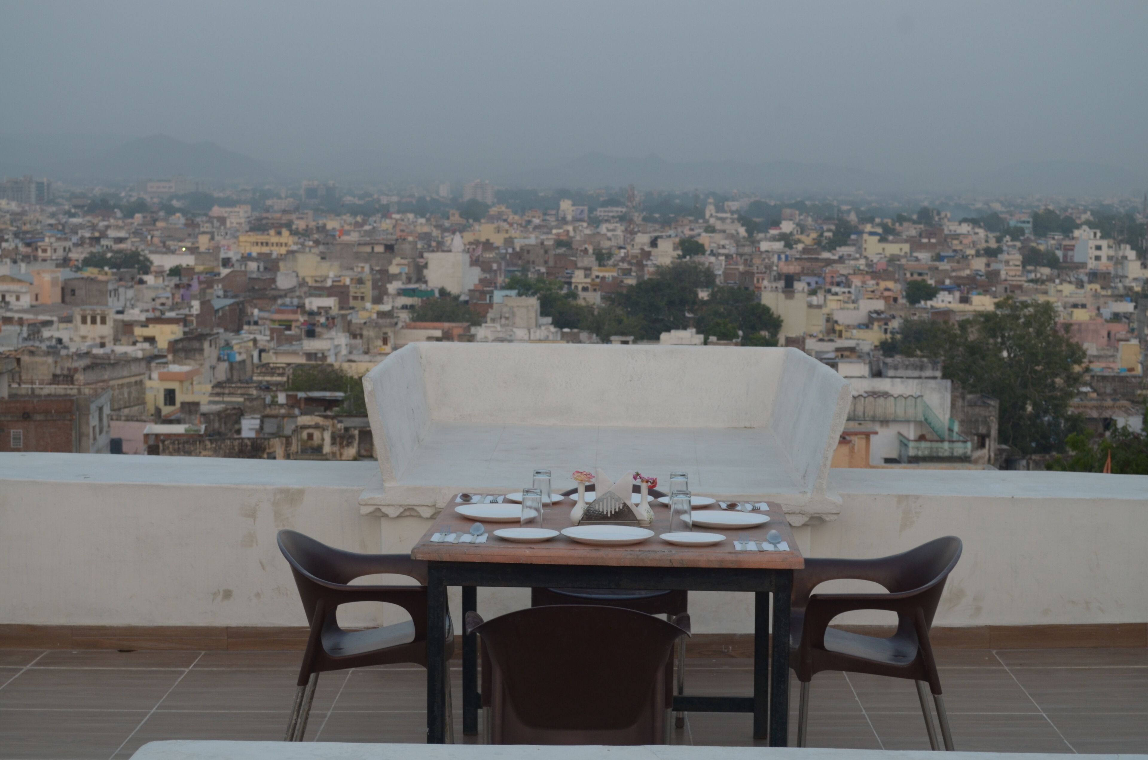 A dining table set on a rooftop with a cityscape view.