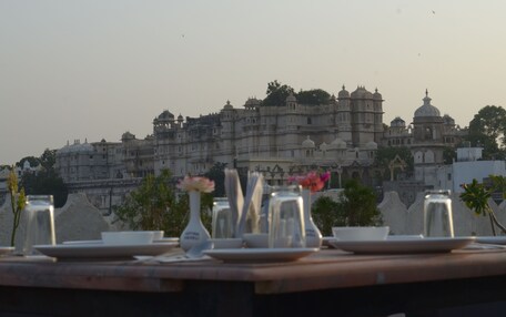 A dining table set with plates, glasses, and vases, with a view of a large, historic building in the background.