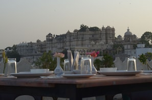 A dining table set with plates, glasses, and vases, with a view of a large, historic building in the background.