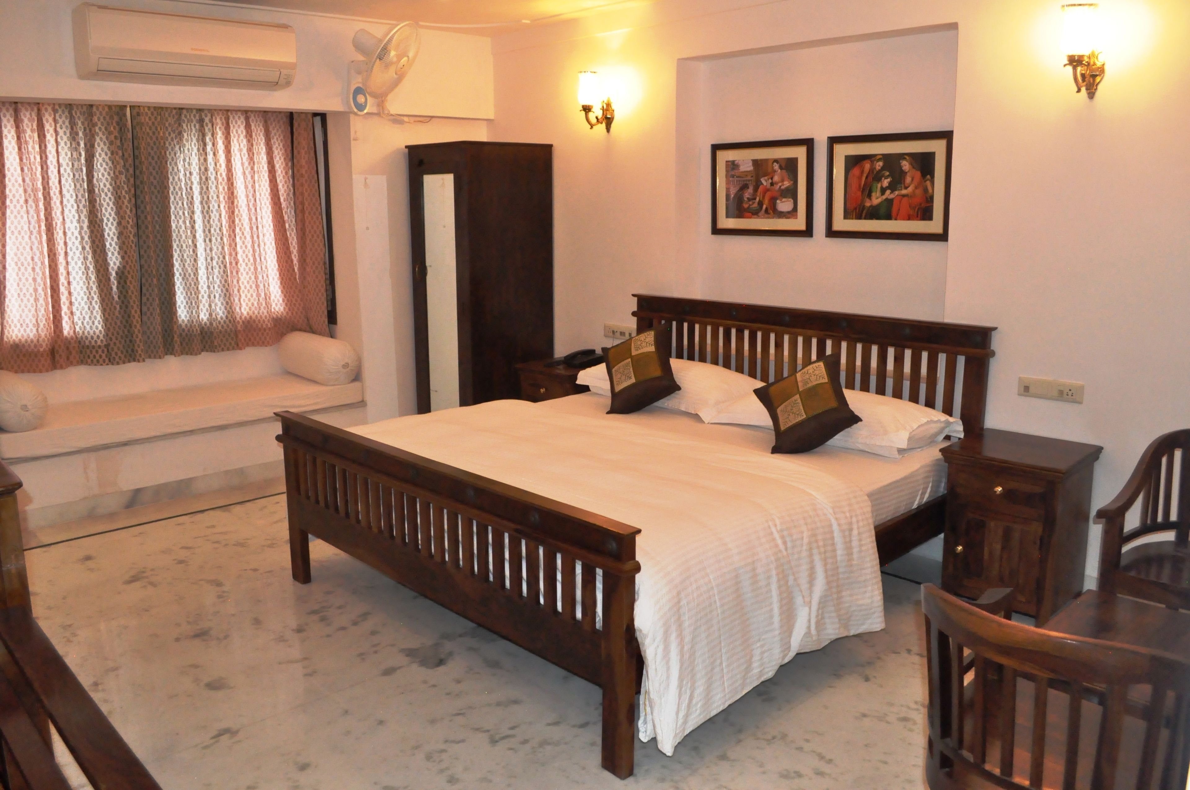 A bedroom with a wooden bed, a nightstand, a chair, a window with curtains, and two wall-mounted lights.