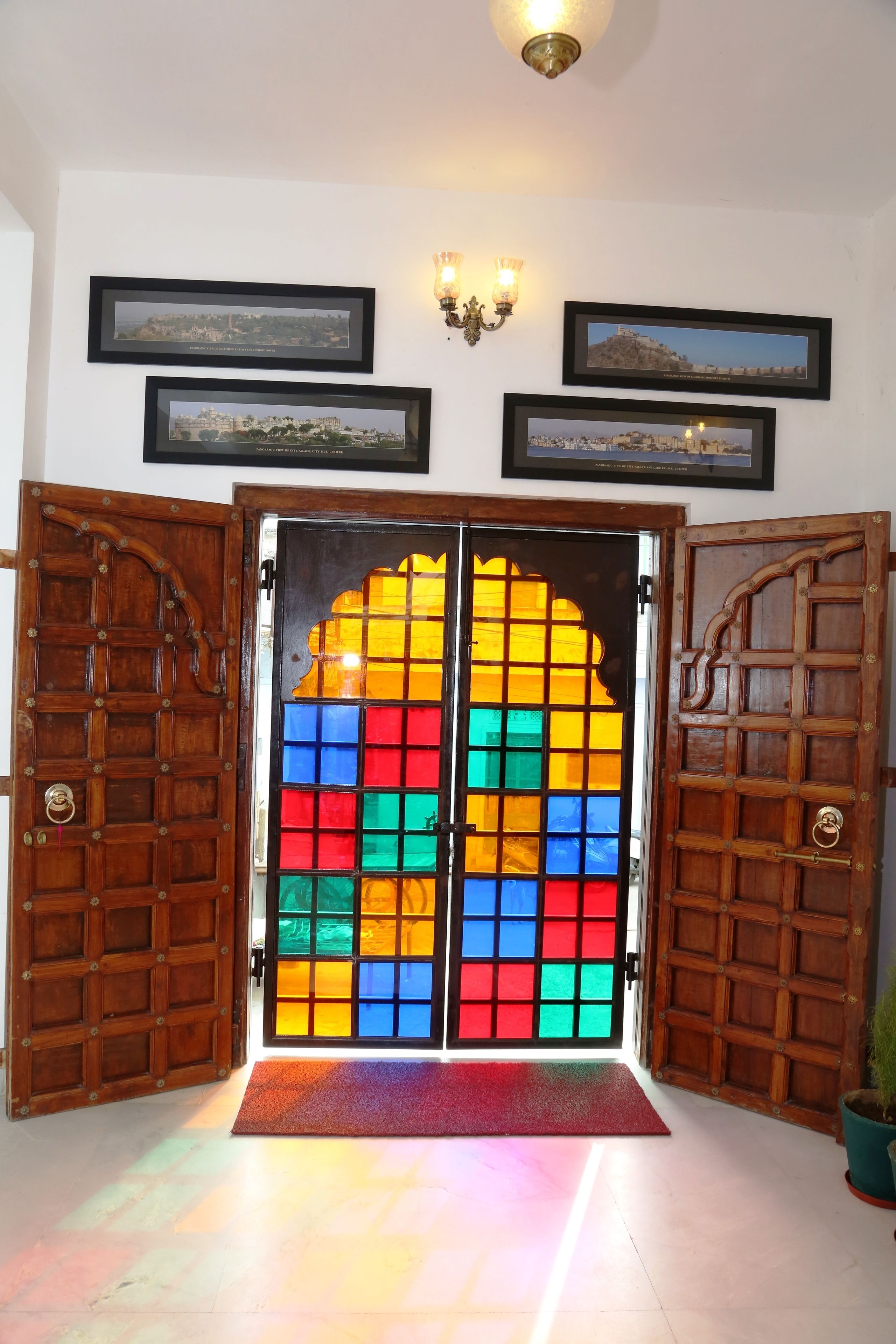 Une porte en bois ornée de panneaux de vitrail aux couleurs vives, un paillasson rouge à l’entrée et des tableaux encadrés accrochés au mur.