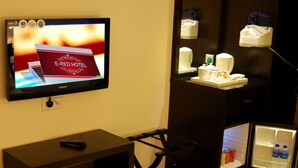 Une chambre d’hôtel équipée d’une télévision affichant le logo de l’hôtel E-Red, d’un mini-réfrigérateur contenant des boissons, d’une machine à café et d’une petite table avec une télécommande.