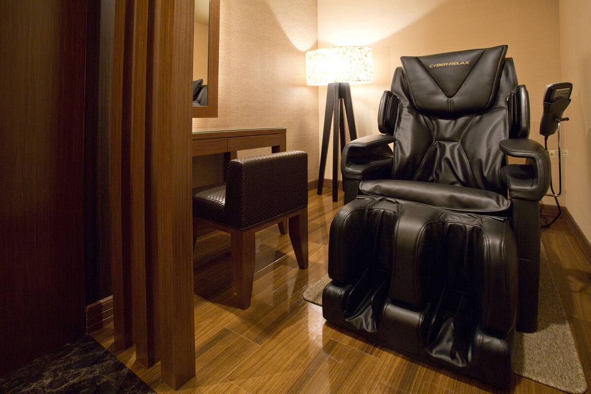 Una silla de masaje, una mesita y una lámpara en una habitación con suelo de madera.
