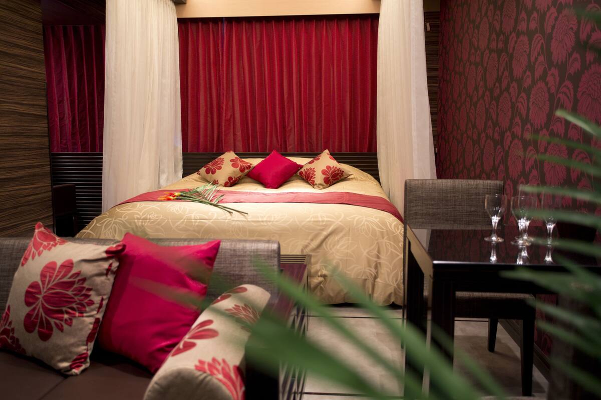Un dormitorio con cama, almohadas, una mesita de noche y cortinas.