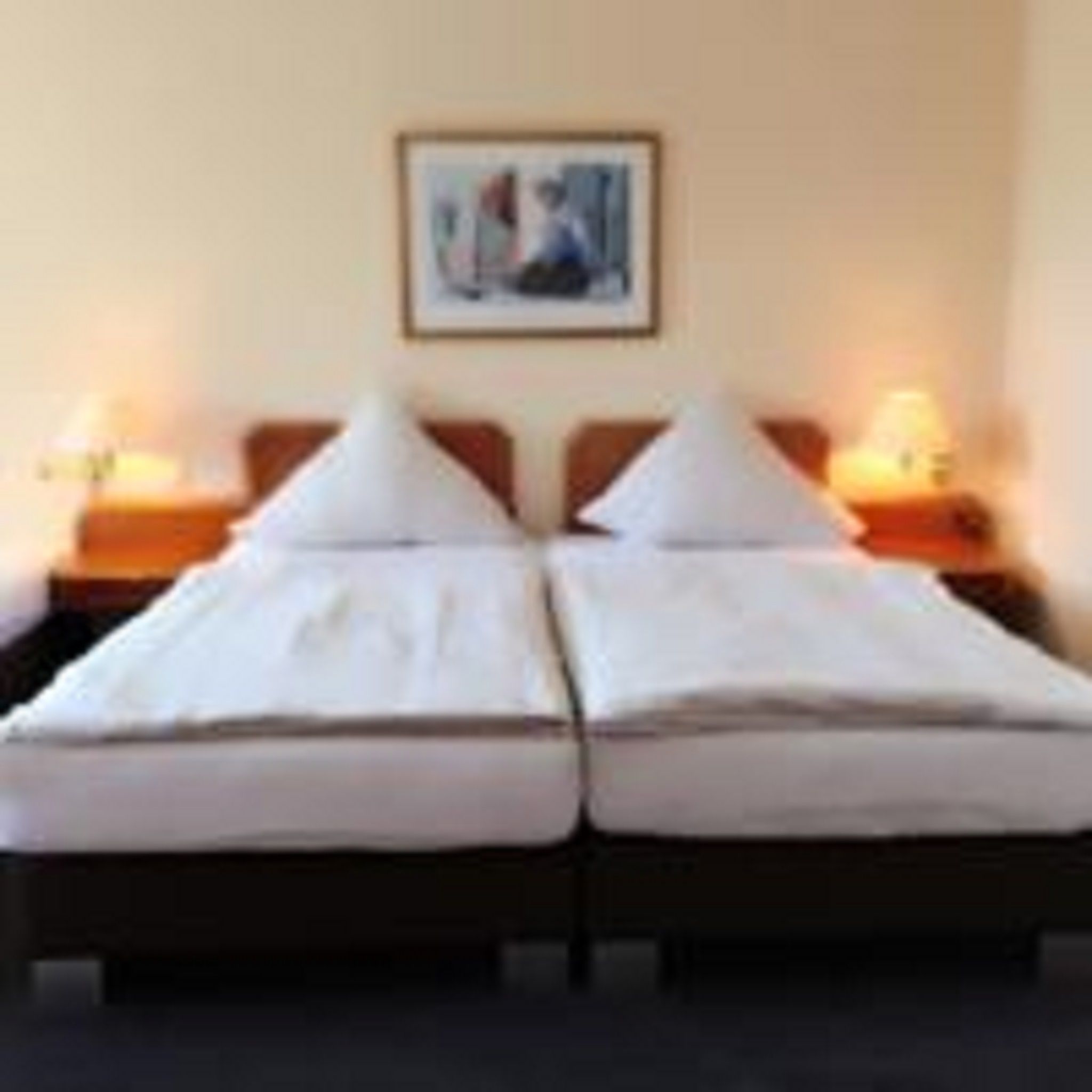 A double bed with white linens, two bedside tables with lamps, and a framed picture on the wall.