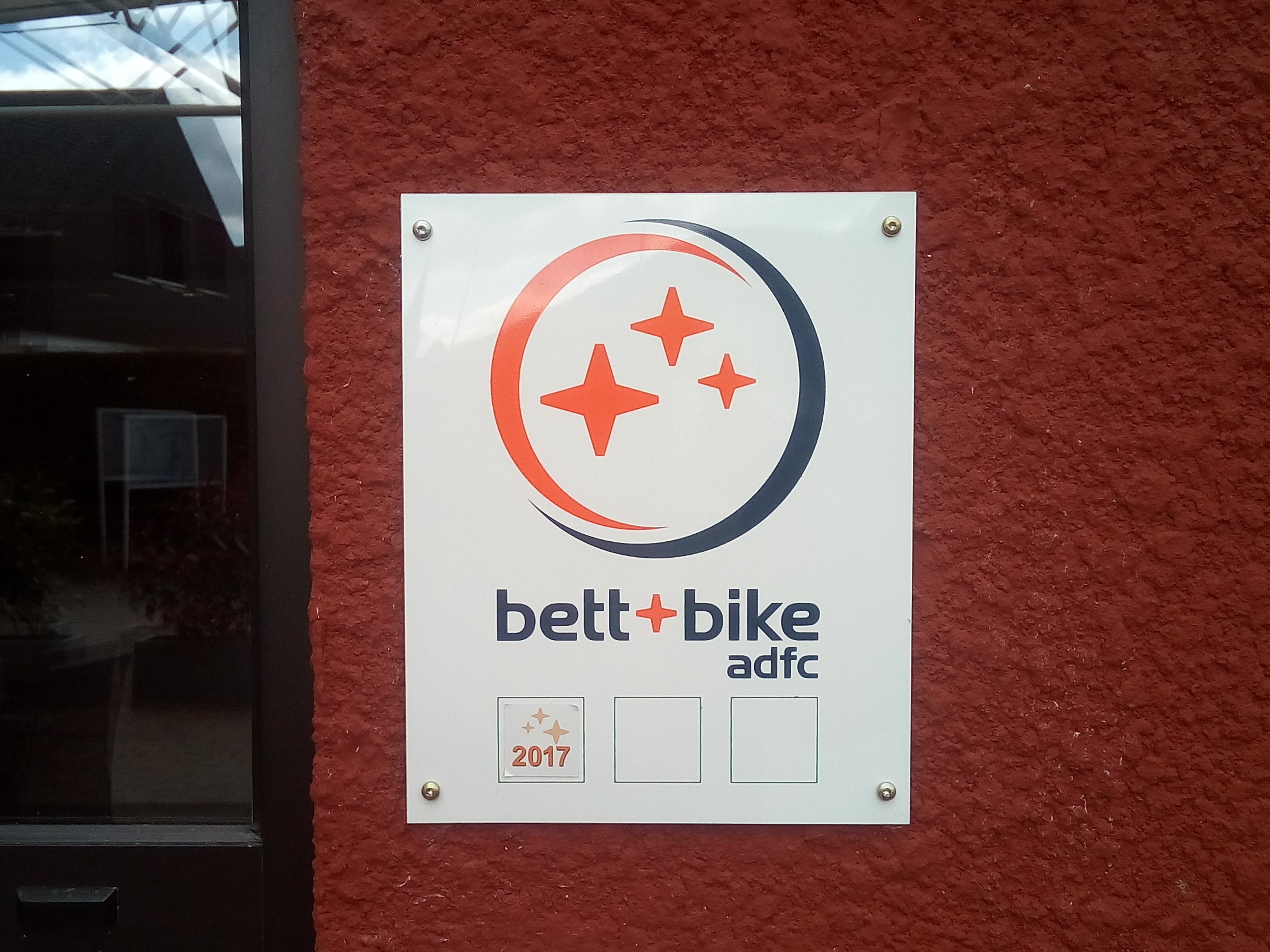 A sign with a logo and text for 'belt+bike adfc' mounted on a red wall.