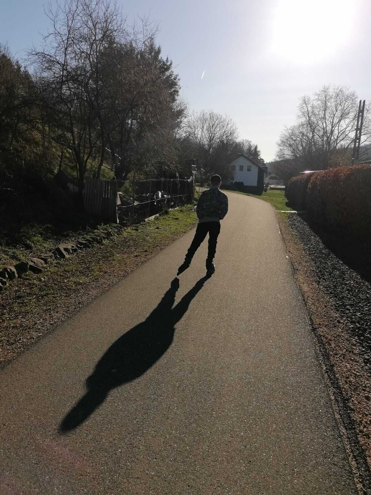 Un chemin pavé sur lequel une personne s’éloigne de la caméra, entourée d’arbres et d’une haie.