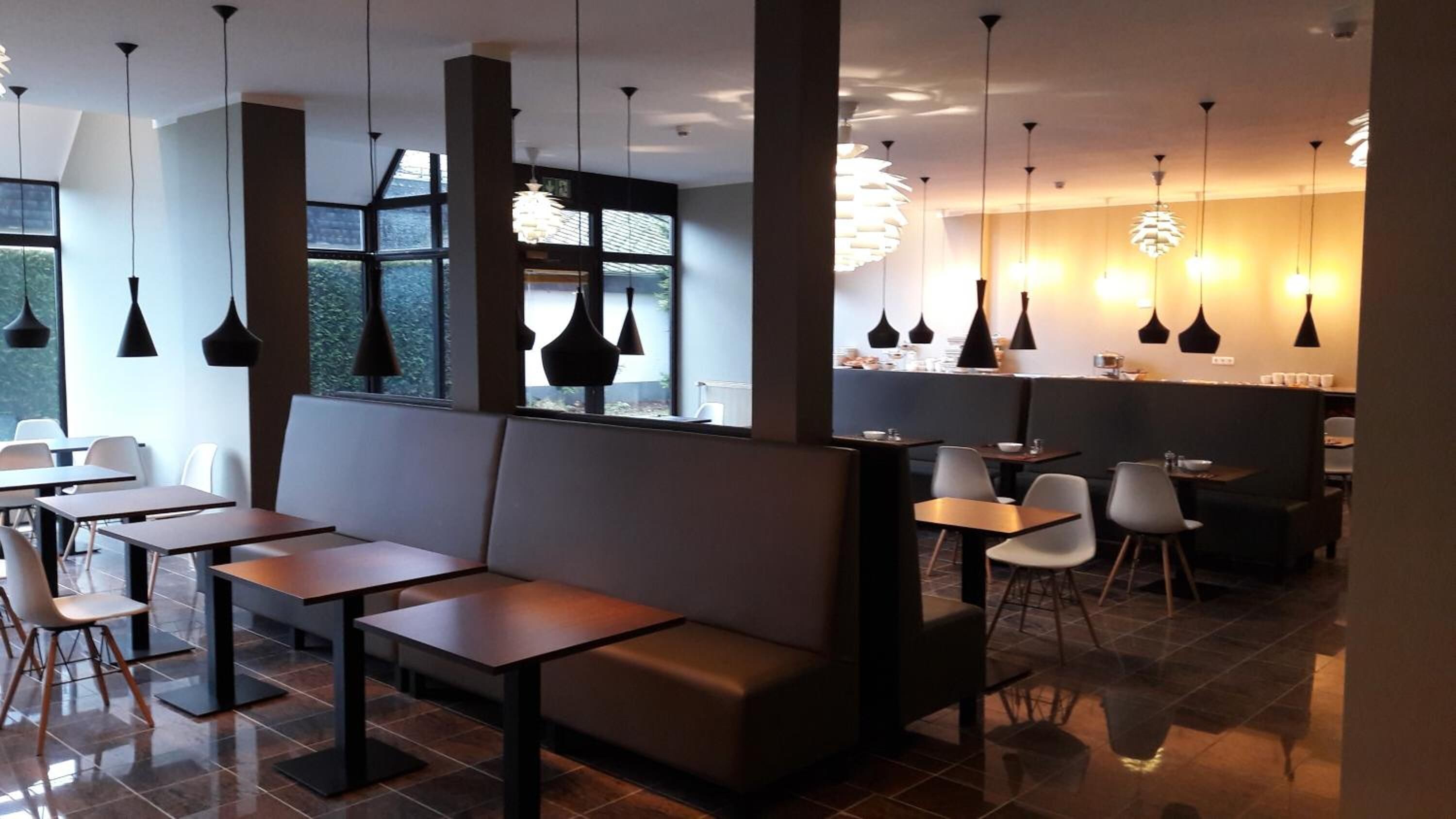 Ein modernes Restaurantinterieur mit hohen Tischen, Bänken und hängenden Pendelleuchten.