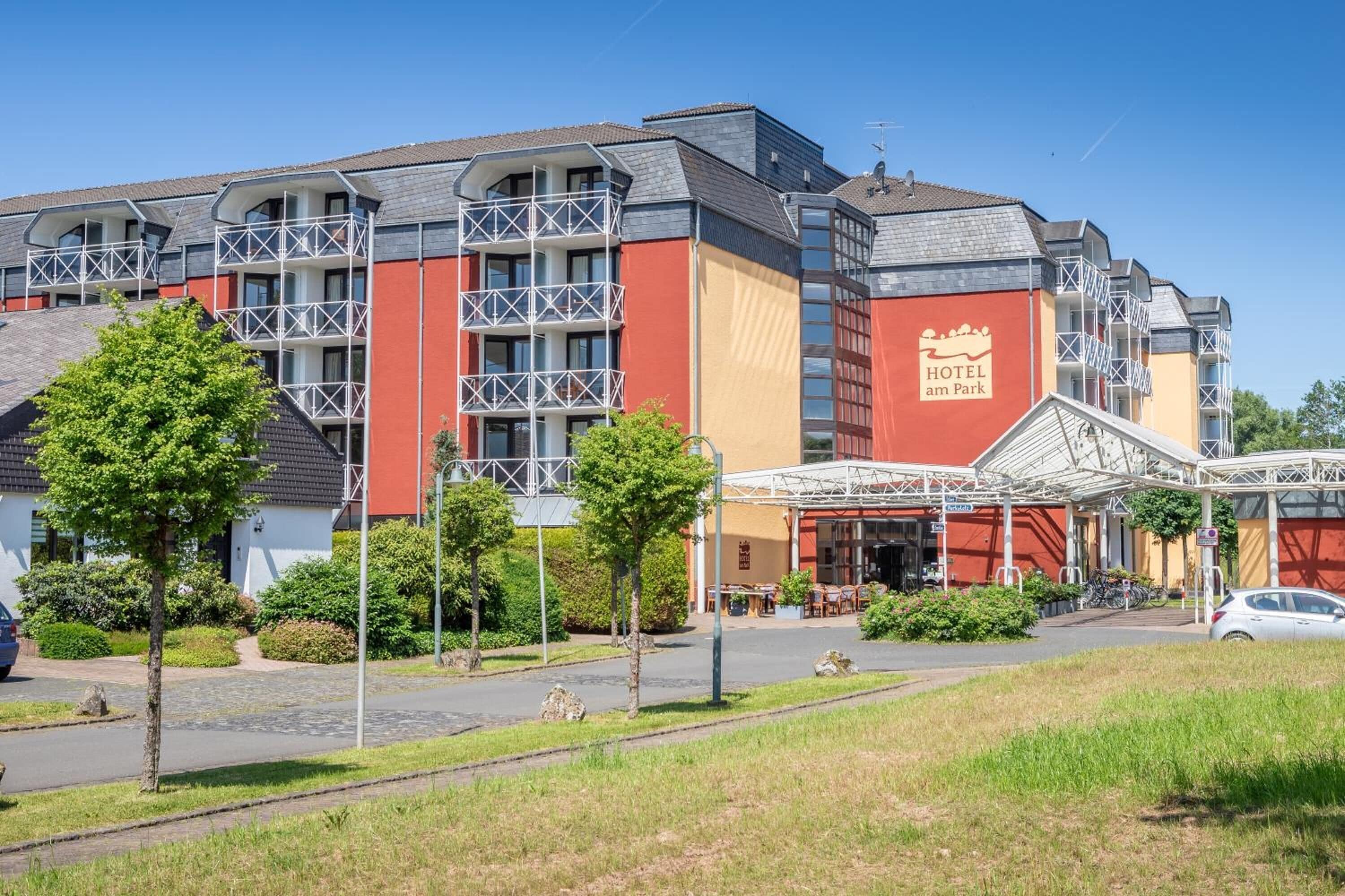 A hotel with a red and beige facade, multiple balconies, and a covered outdoor area with tables and chairs.