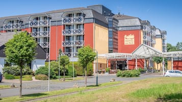 A hotel with a red and beige facade, multiple balconies, and a covered outdoor area with tables and chairs.