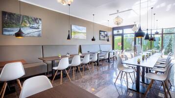 A modern restaurant with high ceilings, large windows, and a mix of seating arrangements including tables and booths.