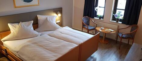 A hotel room with a large bed, two chairs, a small table, and a window with curtains.