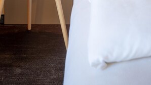 Une chambre d’hôtel avec un lit, une petite table ronde sur laquelle se trouvent une tasse et une plante, et un luminaire fixé au mur.