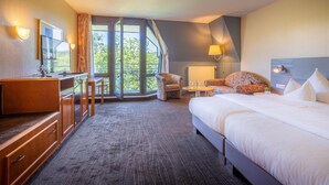 Une chambre d’hôtel avec un grand lit, un bureau avec une chaise, une petite table et une fenêtre avec des rideaux.