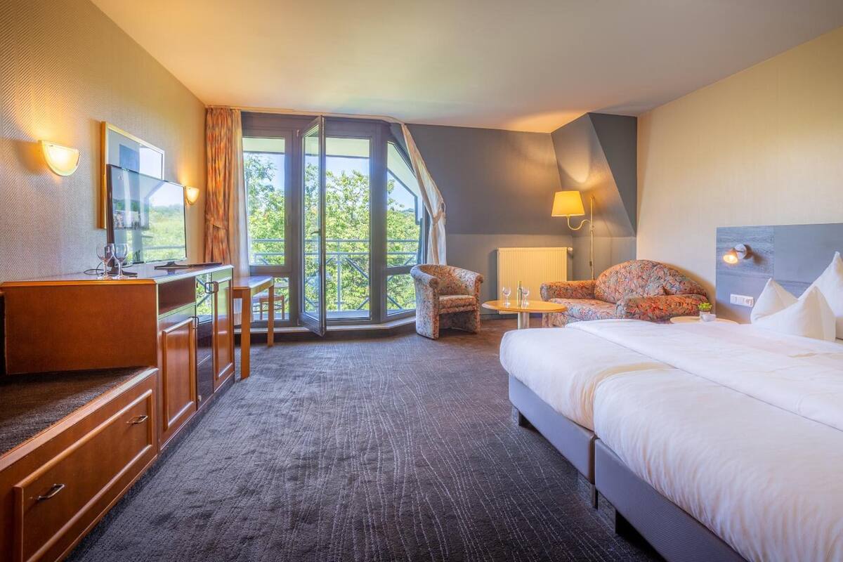 Une chambre d’hôtel avec un grand lit, un bureau avec une chaise, une petite table et une fenêtre avec des rideaux.