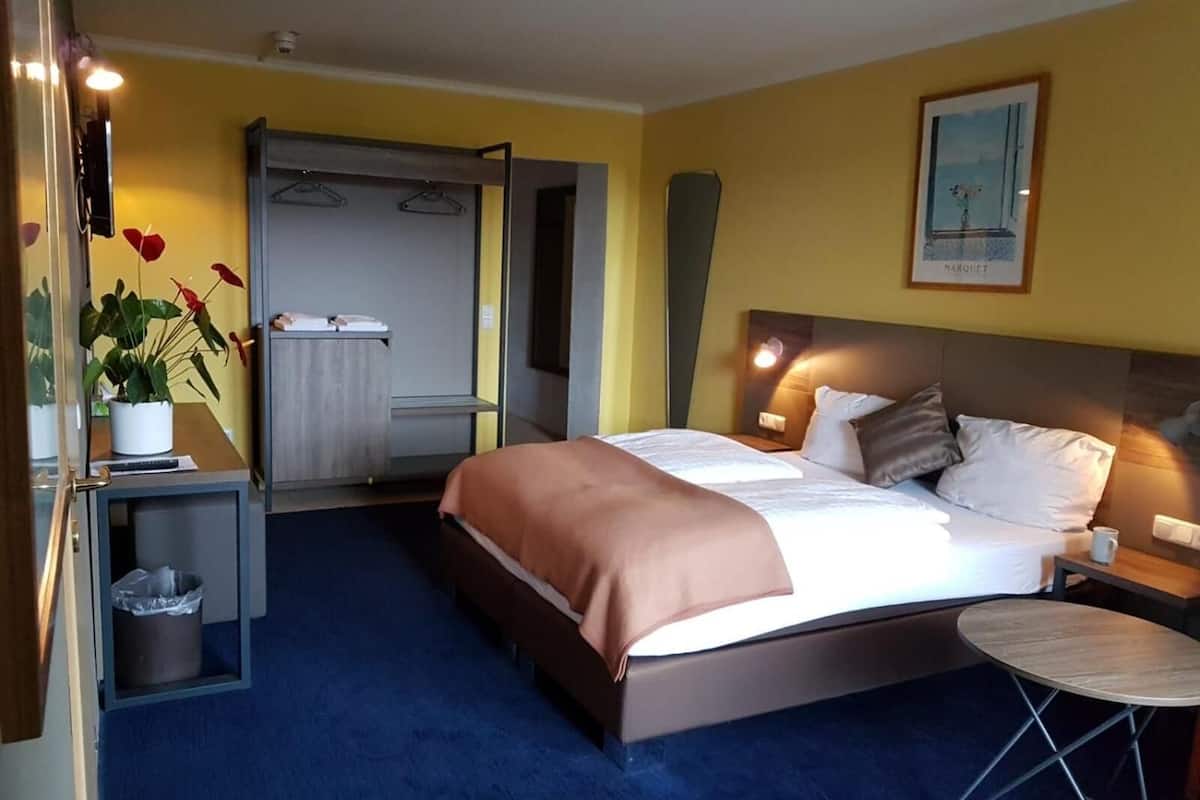 Une chambre d’hôtel avec un lit, une table de chevet, une lampe et une petite table ronde.