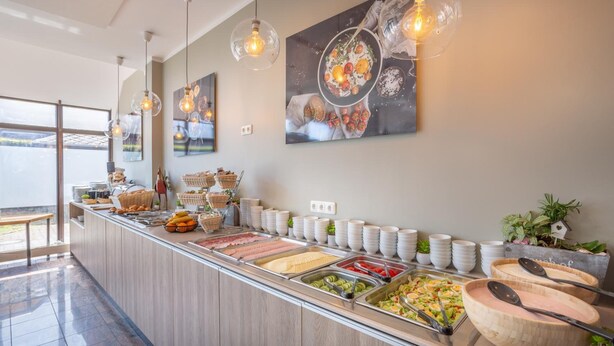 Un buffet proposant une variété de plats et d’ustensiles de service, une grande fenêtre et des luminaires suspendus.