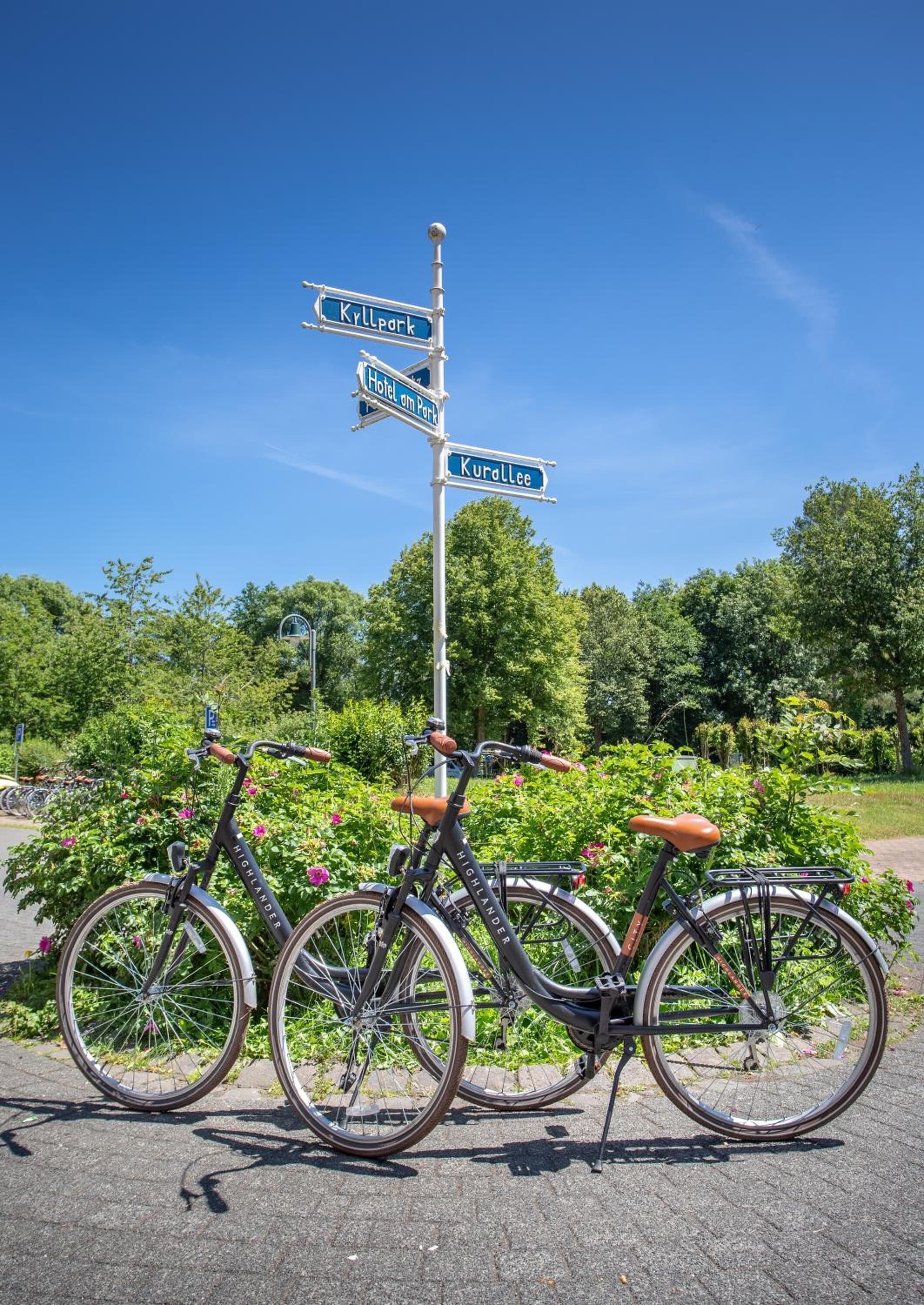 Two bicycles parked next to a signpost with directions to Kyllpork, Hotel en Port, and Kurollee.