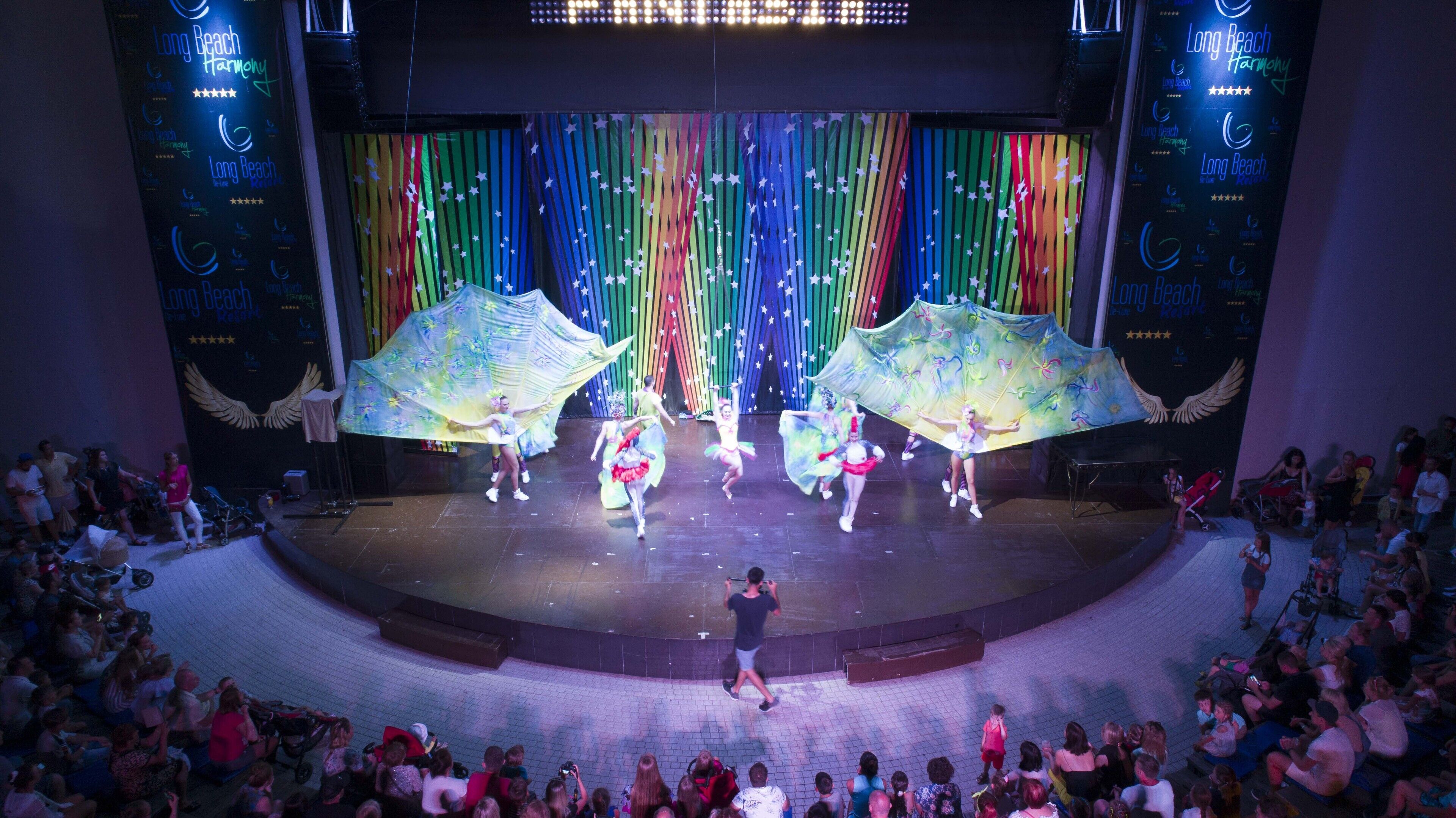 Un escenario con artistas, un público y un fondo decorado con motivos de estrellas.