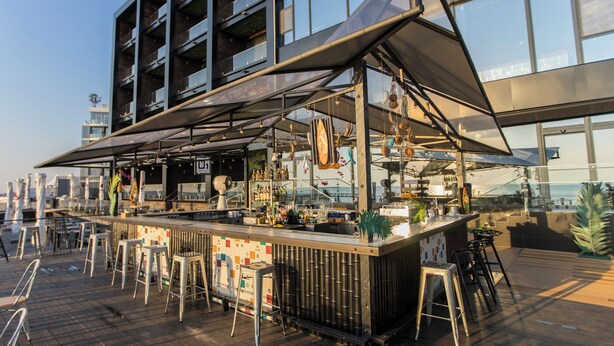 Un bar all'aperto dal design moderno, con un bancone, sgabelli e un grande ombrellone.