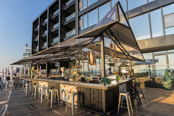 En utomhusbar med modern design, utrustad med en bardisk, barstolar och ett stort parasoll.