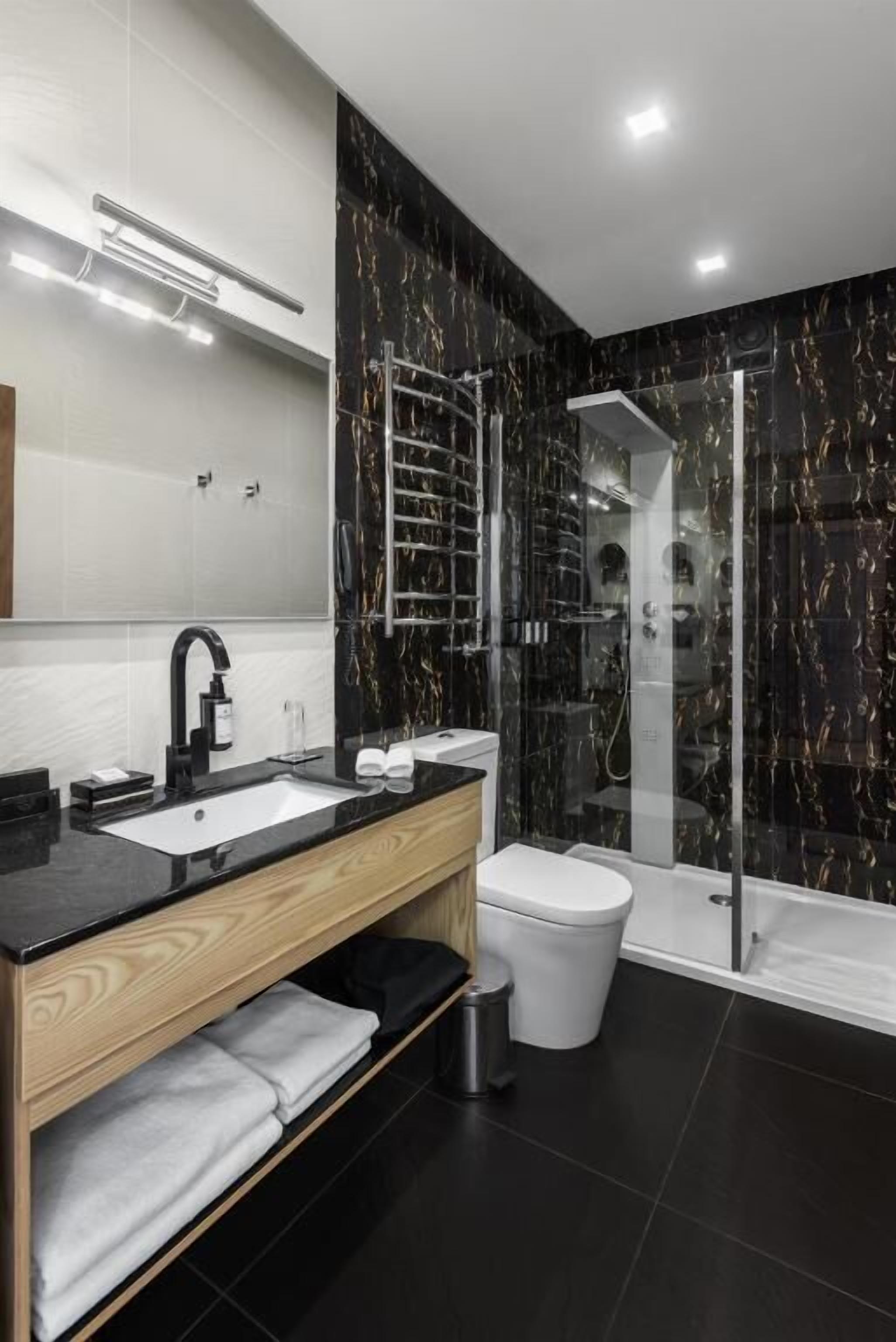 A modern bathroom with a black marble shower, a white toilet, and a wooden vanity with a sink.