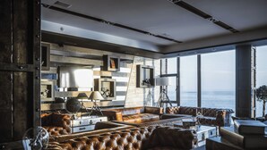 Un soggiorno moderno con una grande finestra vista mare, caratterizzato da divani in pelle, un tavolino da caffè e una libreria.