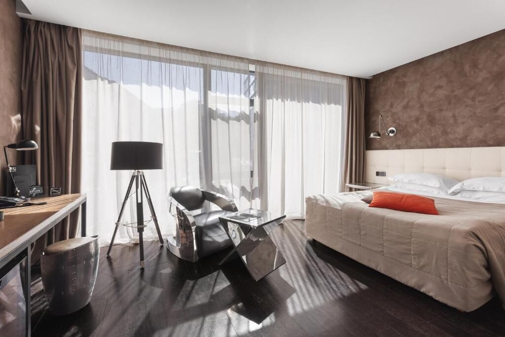 Une chambre d’hôtel moderne avec un grand lit, un bureau avec un ordinateur portable, une chaise et une lampe sur pied.