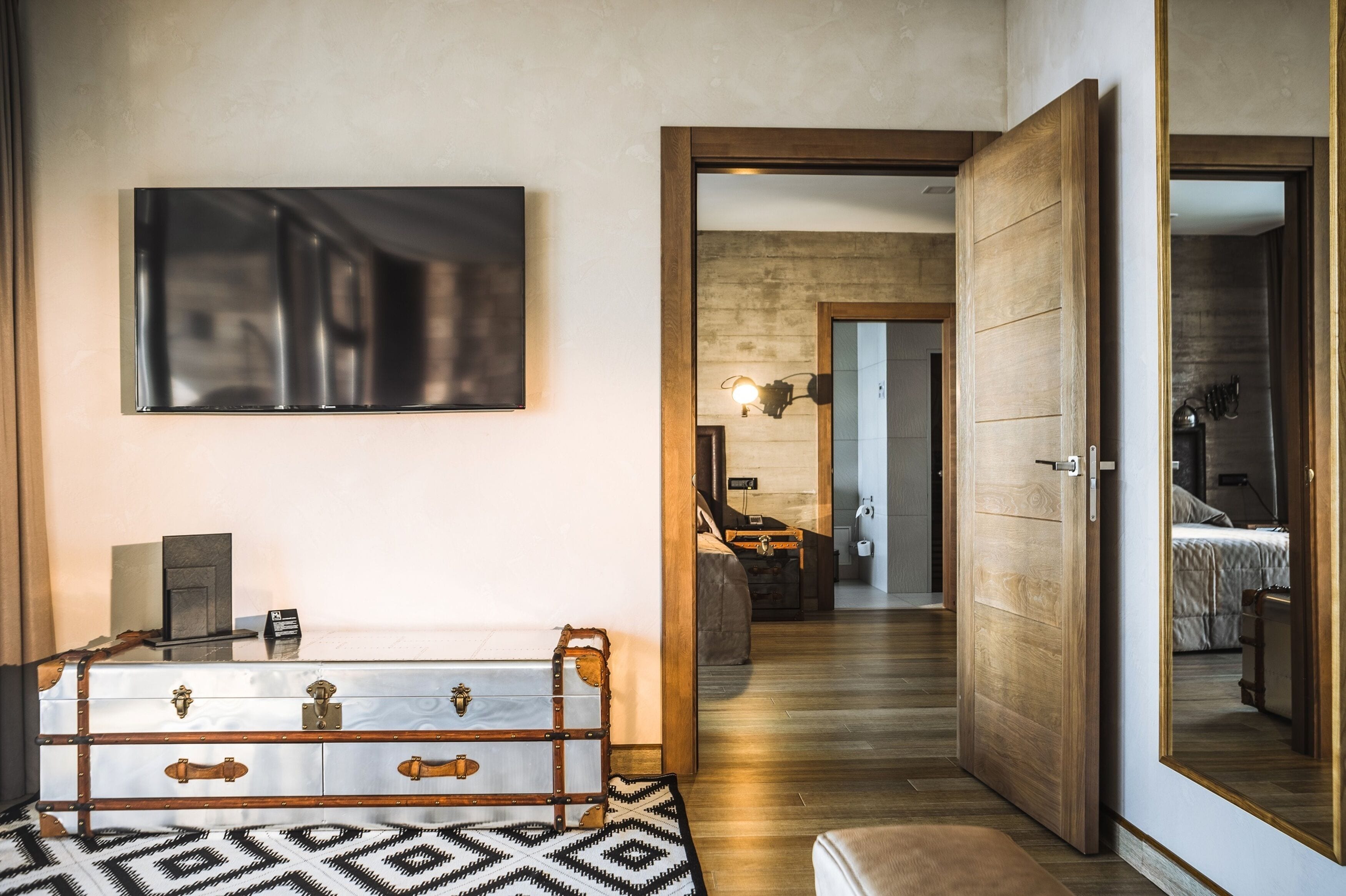 Camera d'albergo moderna con parquet, uno specchio grande, un letto, un comò e una TV a parete.