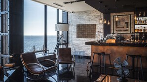 Zona bar moderna con vista sul mare, sgabelli in pelle e un grande cartello di legno che indica un bar della hall.