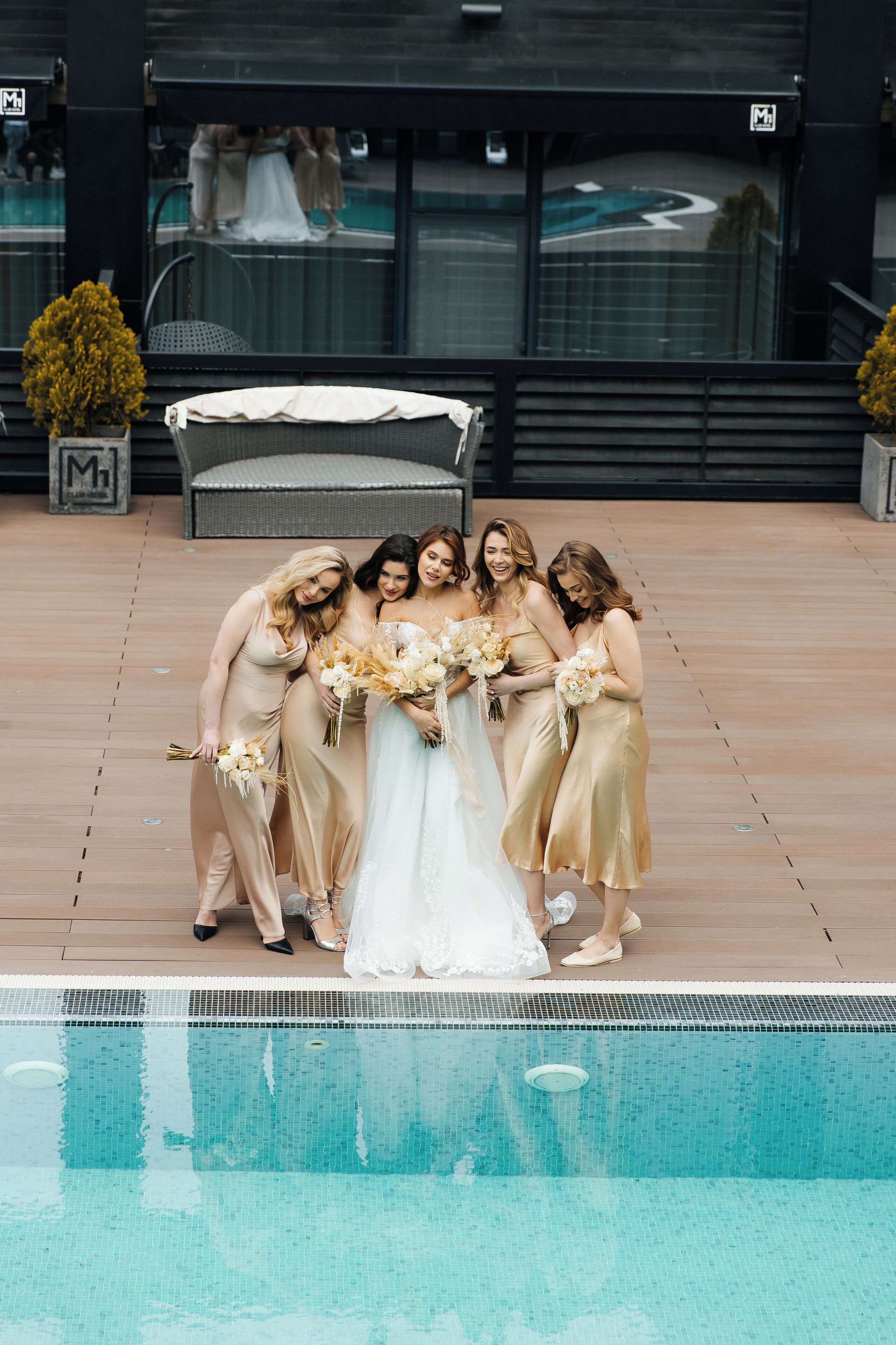 Un grupo de novios junto a una piscina, con un edificio moderno al fondo.