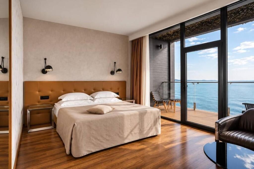 Ein modernes Hotelzimmer mit einem großen Bett, Meerblick und einem Balkon mit einem Stuhl.