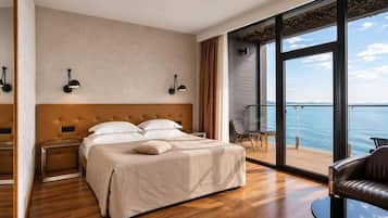 Een moderne hotelkamer met een groot bed, uitzicht op zee, en een balkon met een stoel.