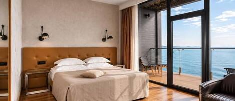 Una habitación de hotel moderna con una cama grande, vistas al mar y un balcón con una silla.