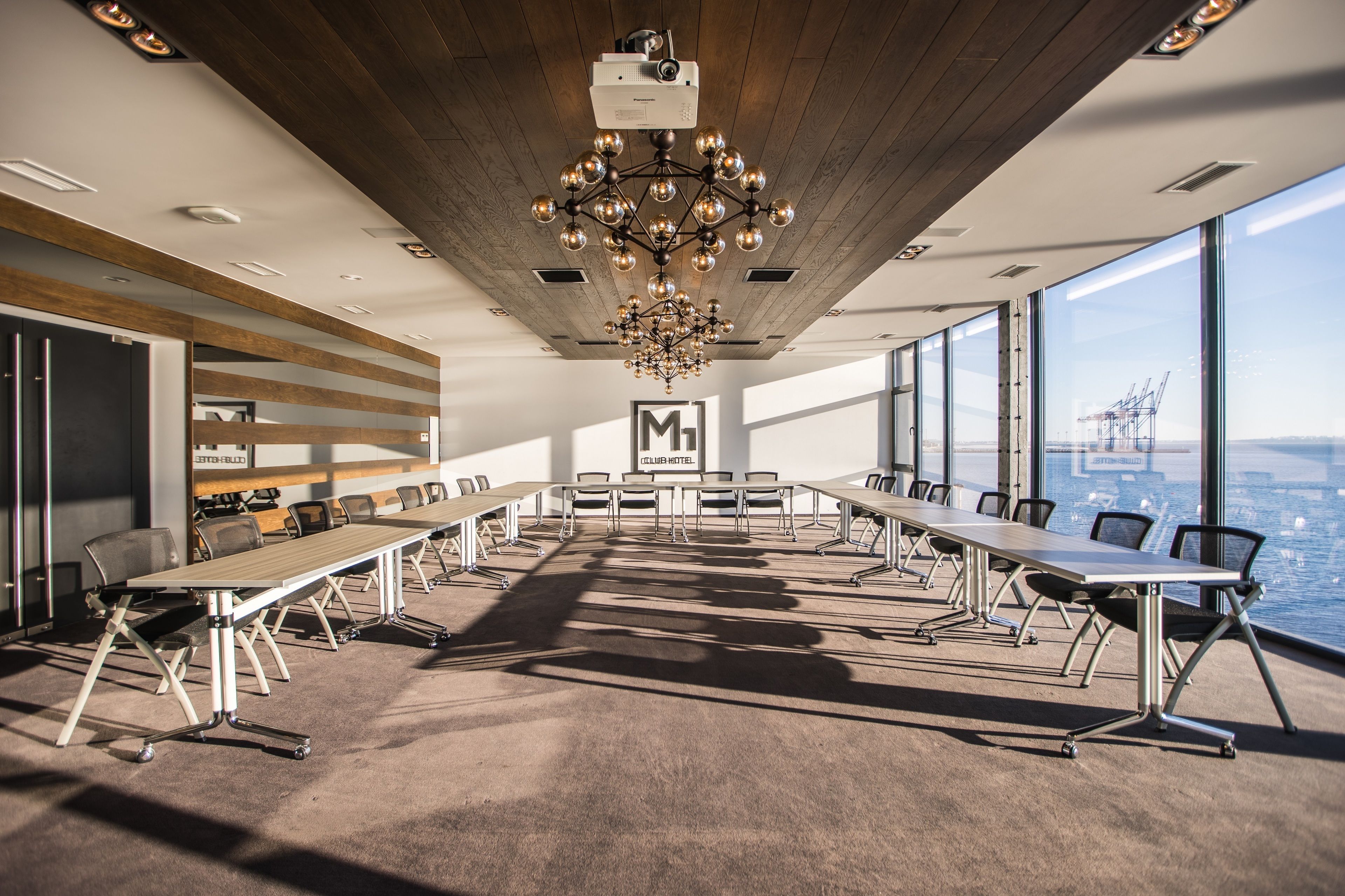 A conference room with a long table, chairs, a chandelier, and large windows overlooking a cityscape.
